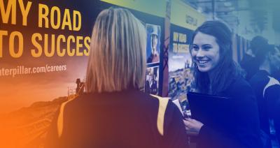 2 women talking, in front of a poster reading my road to success